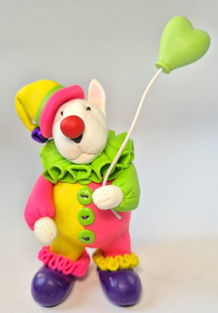 Colorful handmade Bull Terrier clown figurine with a heart balloon. Unique polymer clay collectible gift for Bull Terrier lovers and dog enthusiasts.