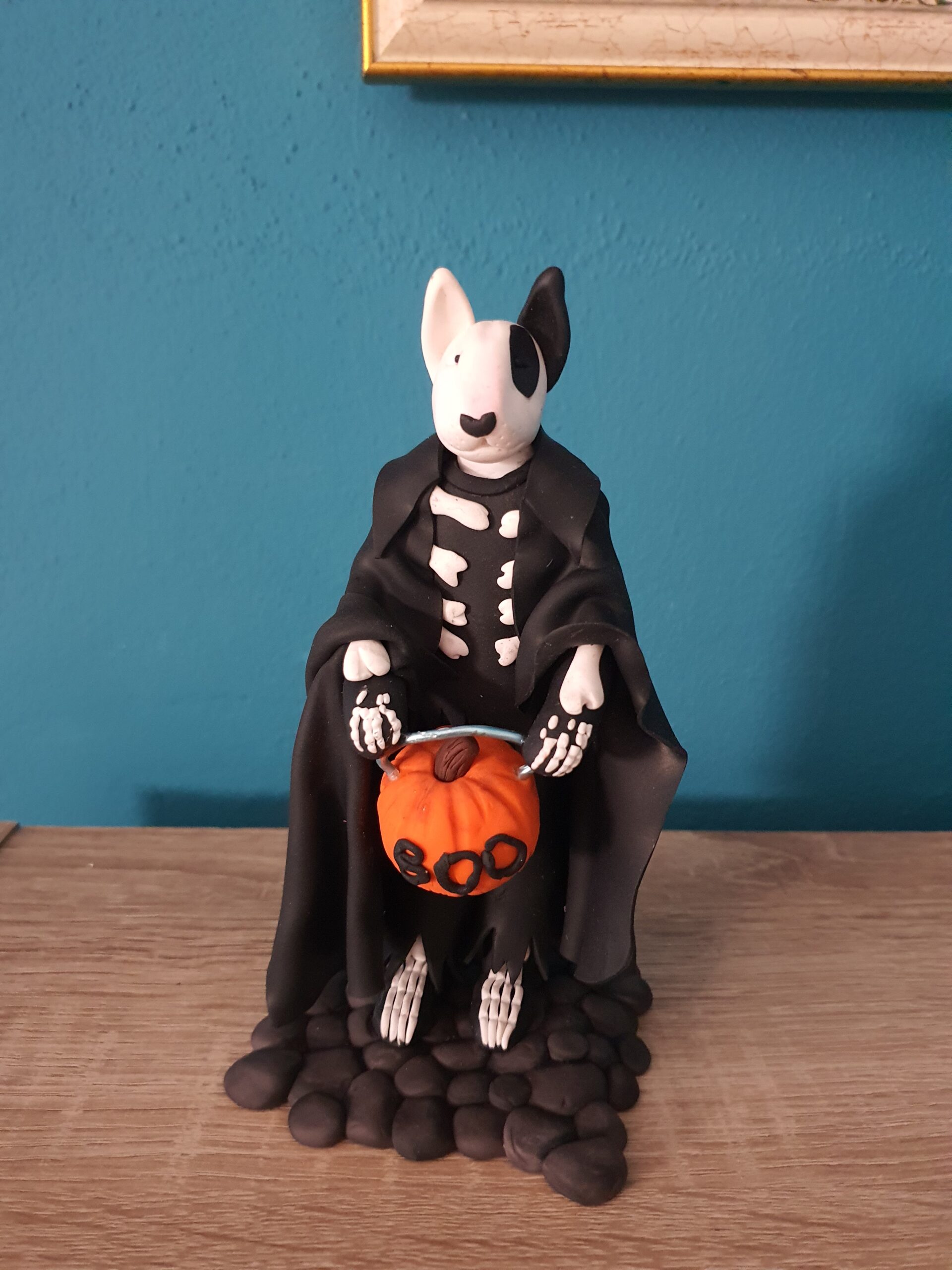 bull terrier in a skeleton costume and holding a pumpkin trick-or-treat bucket.