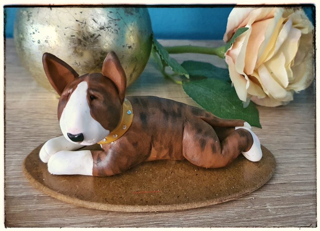 Brindle Bull Terrier figurine lying down on a decorative base